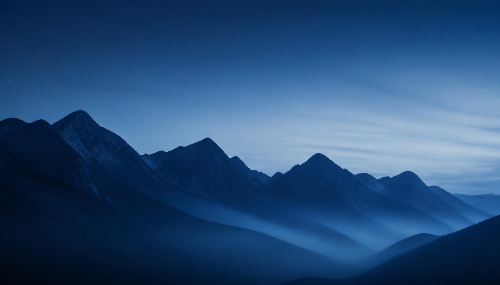 Bergkette mit tiefen Tälern im blauen Morgenlicht als Sinnbild für langfristige Kursverläufe mit zwischenzeitlichen Rückgängen